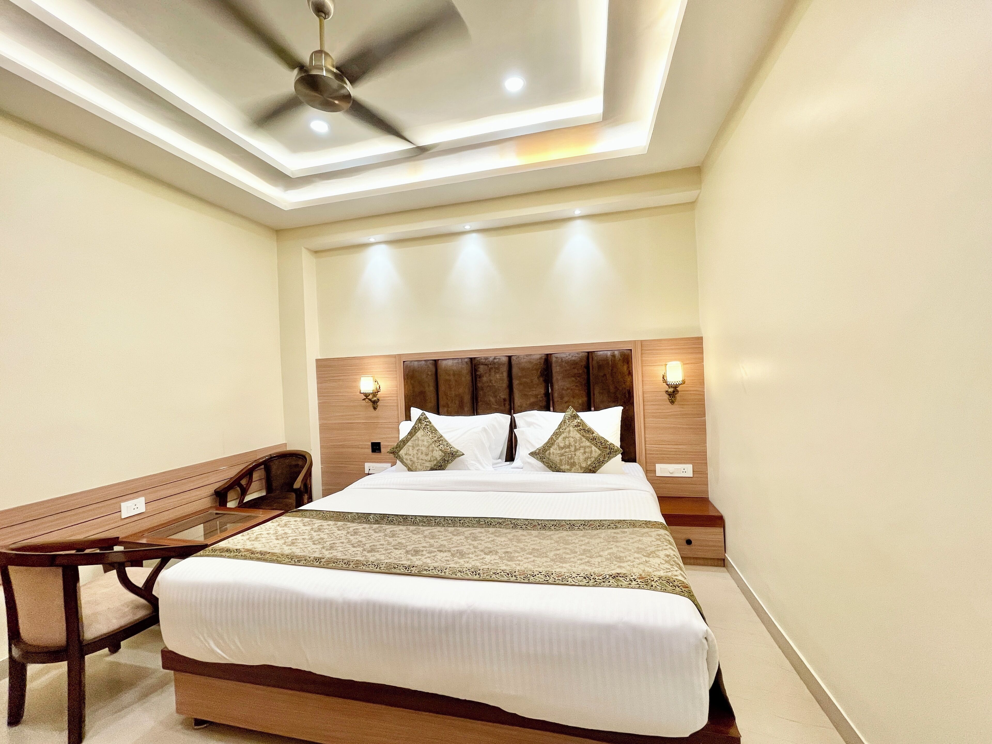 A neatly arranged hotel room with a bed, bedside table, chair, and ceiling fan.