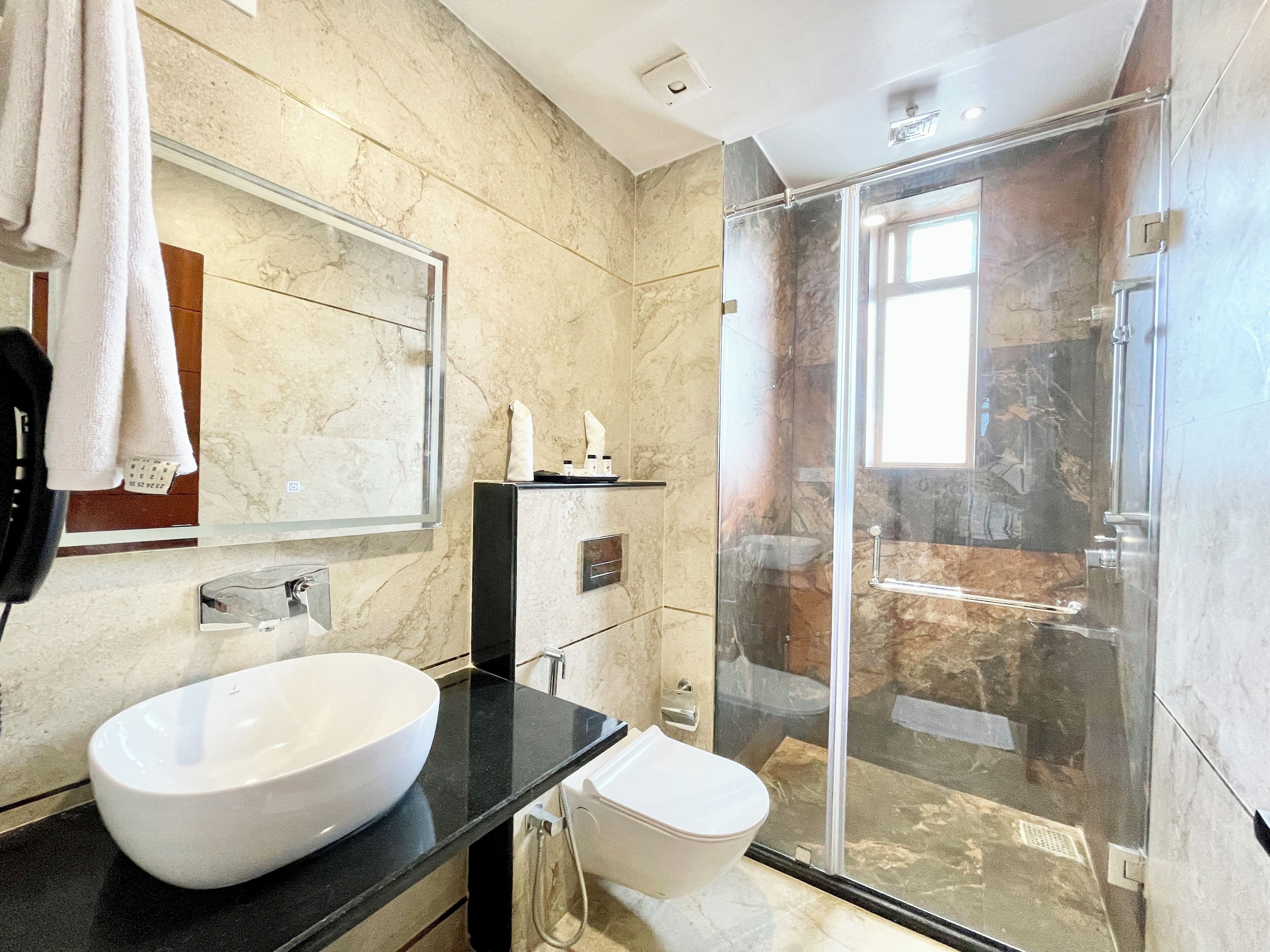 Une salle de bain moderne avec un grand lavabo blanc, une douche en verre et un mur recouvert de carreaux de marbre.
