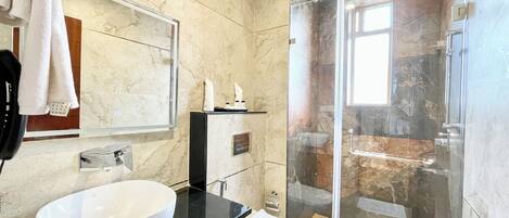 A modern bathroom with a large white sink, a glass shower enclosure, and a marble-tiled wall.