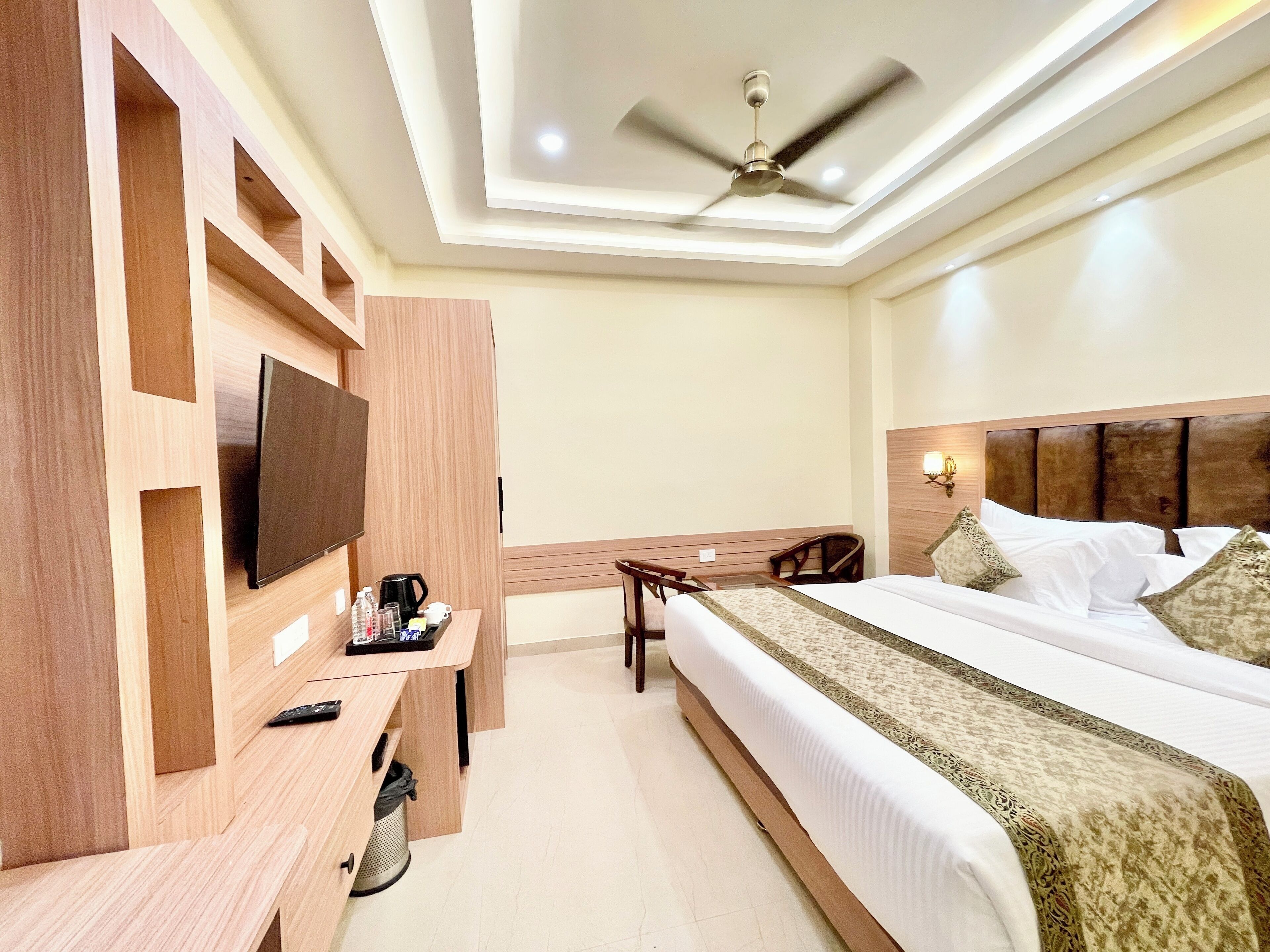 A hotel room with a bed, a desk with a TV, a ceiling fan, and a nightstand.