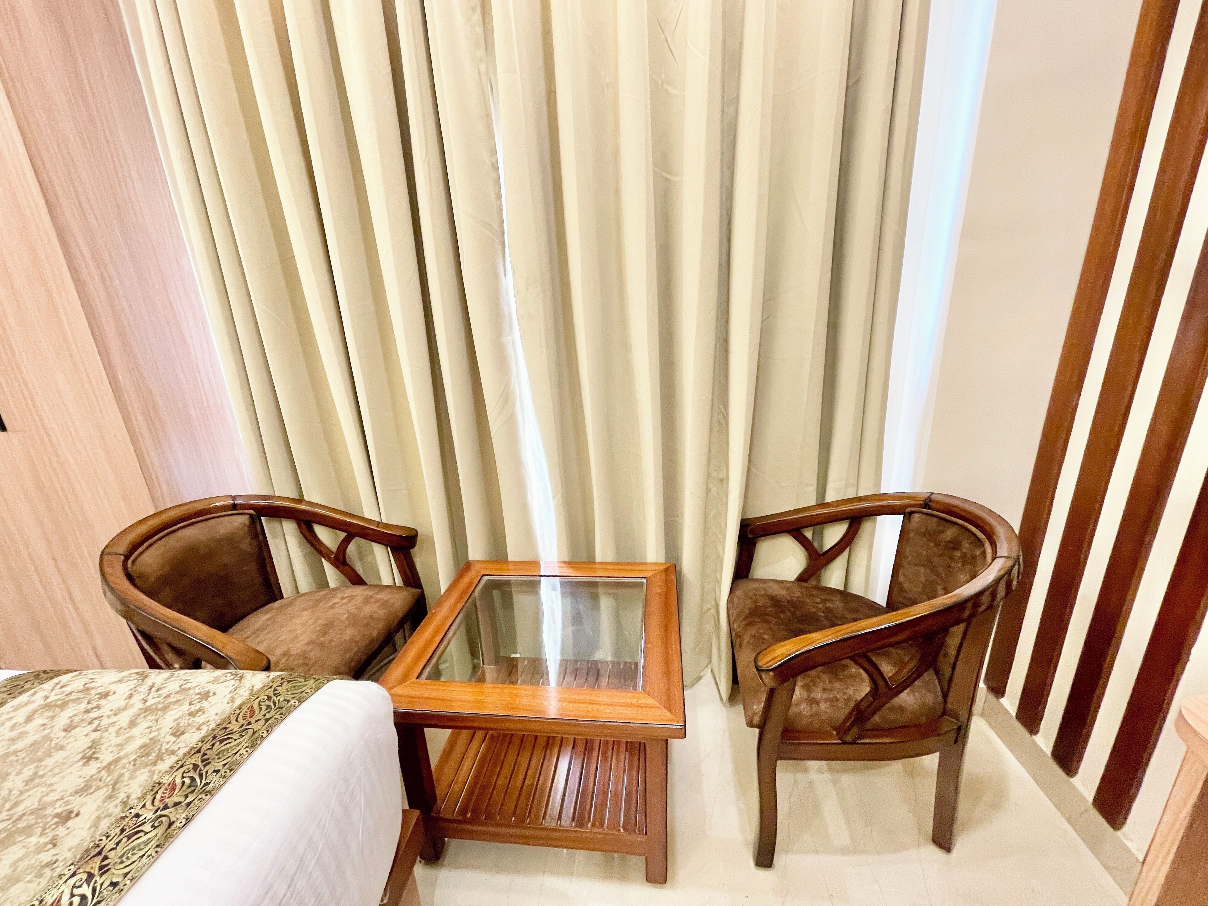 Una habitación con una cama, una mesita de madera, dos sillas y una cortina.