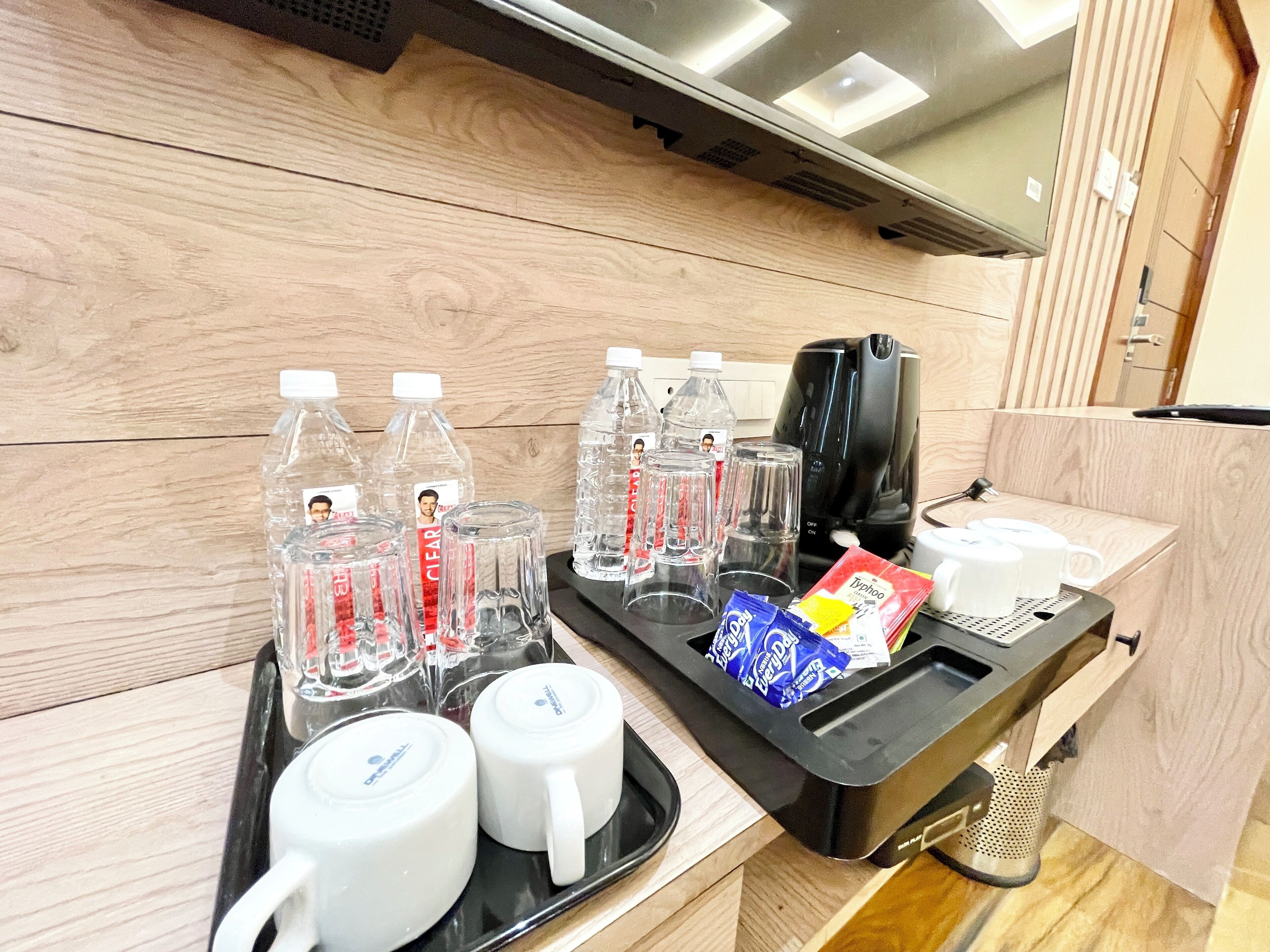 A tray with water bottles, glasses, a coffee maker, and a packet of coffee creamer.