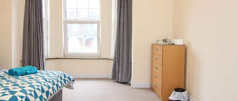 Een slaapkamer met een bed, een houten dressoir, een raam met gordijnen en een vloerbedekking.