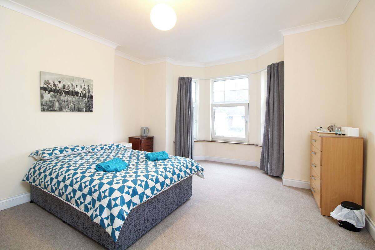 A bedroom with a bed, a dresser, a window with curtains, and a painting on the wall.