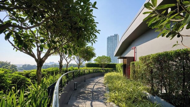 A pathway flanked by greenery and a modern building with a curved facade. - Riva Vibe Hotel Bangkok by PCL (Bangkok)