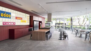 A modern restaurant with a long wooden table, red walls, and a large window offering a view of the outdoors. - Riva Vibe Hotel Bangkok by PCL (Bangkok)