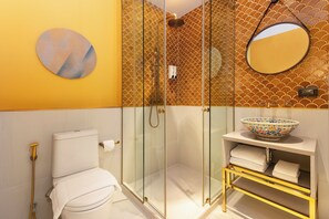 Een badkamer met een glazen douchecabine, toilet, wastafel met een decoratieve kom en een spiegel aan de muur.