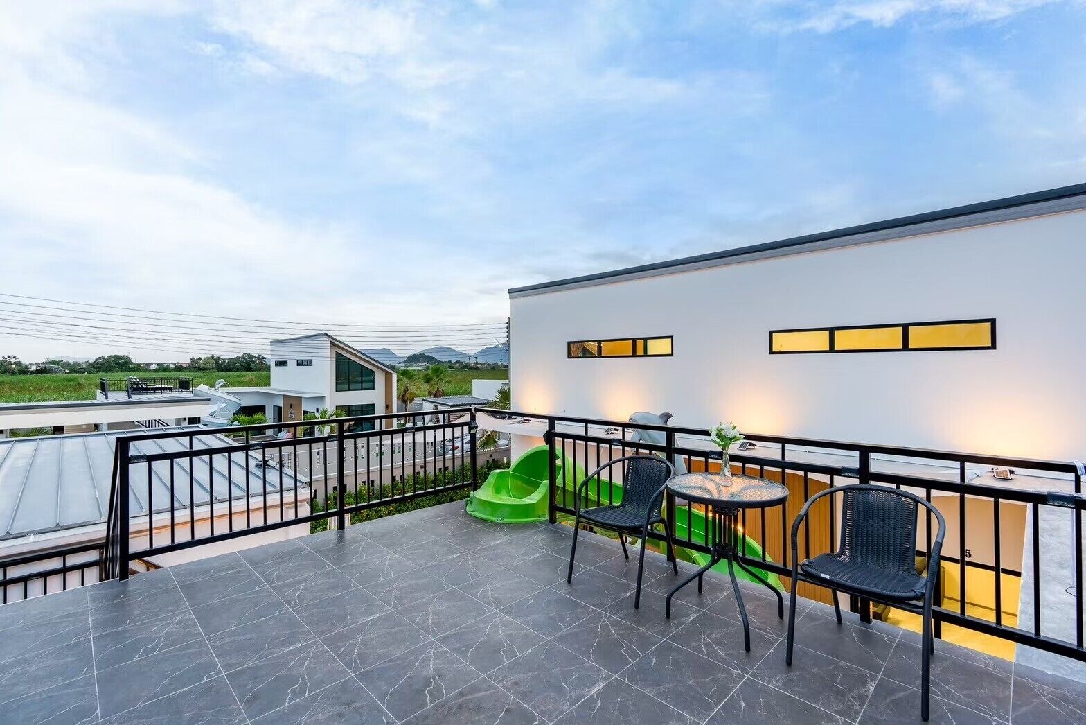 Une terrasse extérieure moderne, dotée d’une balustrade en métal noir, d’une chaise verte et d’une table ronde avec des chaises.