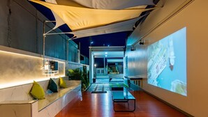 A modern hotel lobby with a wooden floor, a reception desk, a seating area with cushions, and a large screen displaying a map. - 58-20 Pool Villa (Cha-am)
