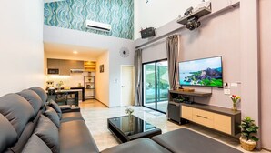 A modern living room with a black sofa, a glass coffee table, and a flat-screen TV mounted on the wall. - 58-20 Pool Villa (Cha-am)