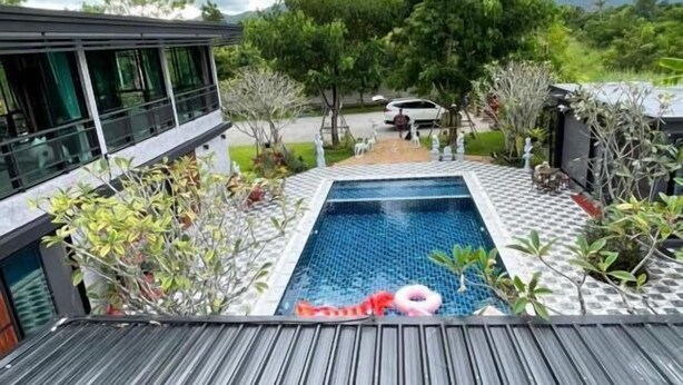 A modern pool area with a wooden deck, surrounded by lush greenery and a cloudy sky. - Intouch Poolvilla (Cha-am)
