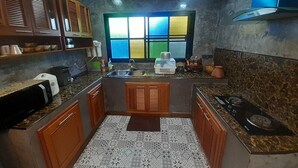 A compact kitchen with wooden cabinets, a built-in microwave, a gas stove, and a window with a colorful view. - Intouch Poolvilla (Cha-am)