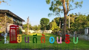 A garden with a red telephone booth and a sign with colorful letters spelling out a name. - Intouch Poolvilla (Cha-am)