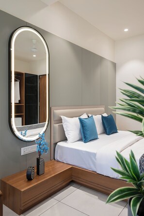 A modern bedroom with a large mirror, bedside table, and a bed with blue pillows. - The Zuree Hotel (Gandhinagar)
