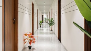 A long, well-lit hallway with wooden doors on either side, potted plants, and a shiny tiled floor. - The Zuree Hotel (Gandhinagar)