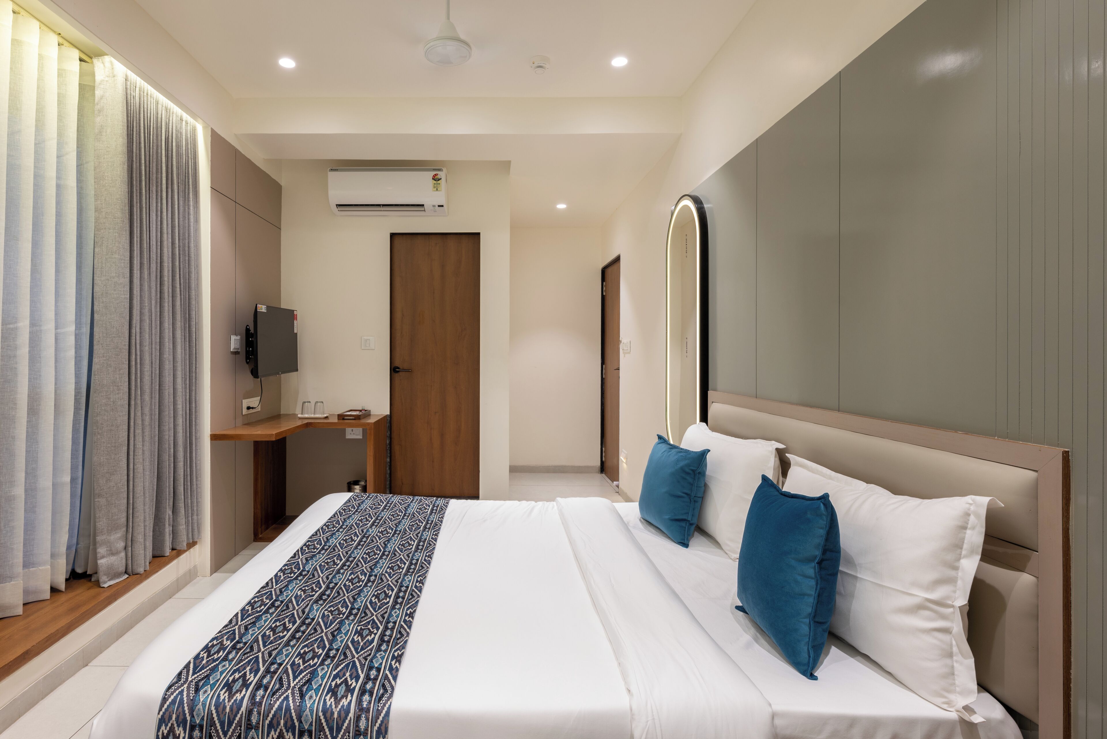 A modern hotel room with a large bed, a bedside table, a flat-screen TV, and an air conditioning unit on the wall.