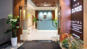 A hotel reception area with a modern design, featuring a reception desk, glass doors, and potted plants. - The Zuree Hotel (Gandhinagar)