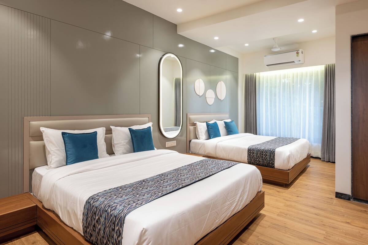 A modern hotel room with two beds, a large mirror, and a ceiling air conditioner.