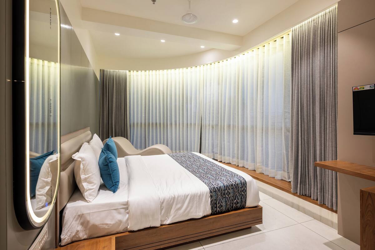 A modern bedroom with a bed, a bedside table, a mirror, and a TV on the wall.