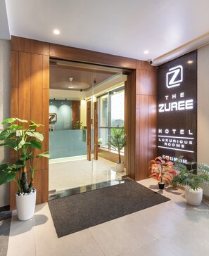 A hotel entrance with a glass door, wooden paneling, and a sign for "The Zuree Hotel Luxury Rooms." - The Zuree Hotel (Gandhinagar)