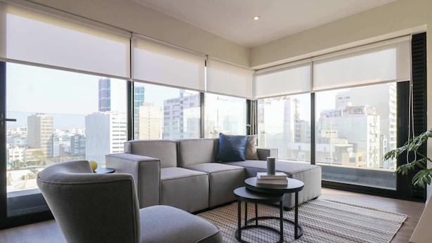 A modern living room with a sectional sofa, a round coffee table, and a large window offering a city view. - w* | Exlusive 3BR w/ Balcony Near Larcomar (Miraflores)