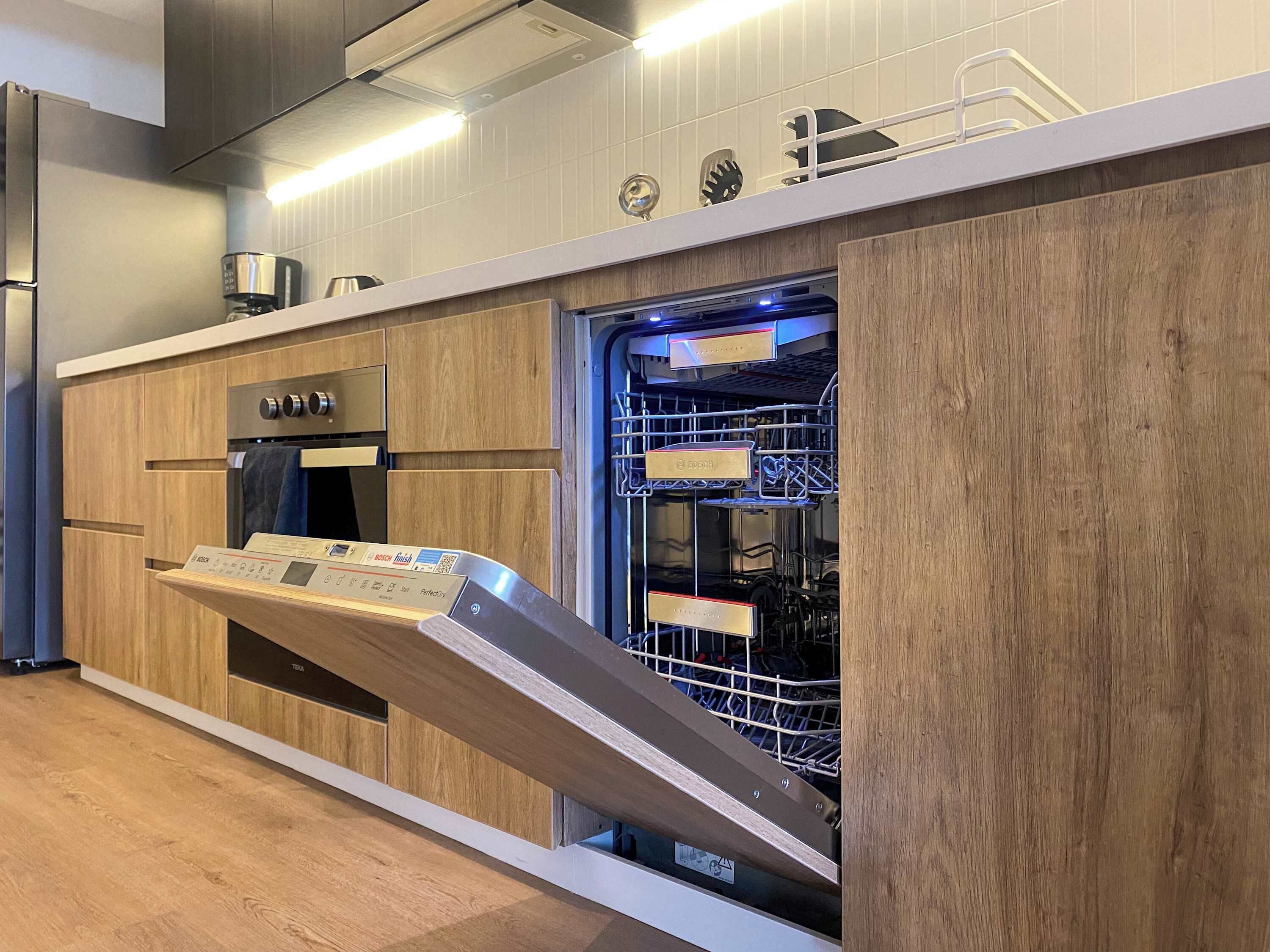 A modern kitchen with a built-in dishwasher, wooden cabinets, and stainless steel appliances.