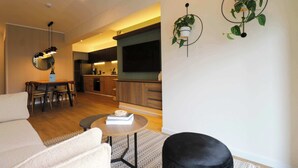 A modern living room with a sofa, a coffee table, and a dining area with chairs. There is a kitchen in the background with wooden cabinets and a TV mounted on the wall. - w* | Elegant 2BR w/ Balcony Near Larcomar (Miraflores)