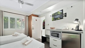 Habitación de hotel con dos camas, un escritorio con microondas, refrigerador, ventilador de techo y televisor en la pared.