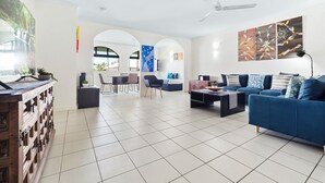 Amplia sala de estar con un sofá azul, una mesa de centro y un televisor. Hay una zona de comedor con sillas y una mesa, y una cocina con estufa.