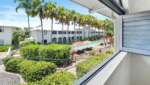 Vista de un patio de hotel con palmeras, piscina y un edificio con ventanas arqueadas.