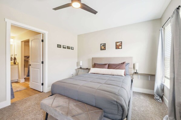 A bedroom with a bed, a bench, a ceiling fan, and a nightstand with a lamp.
