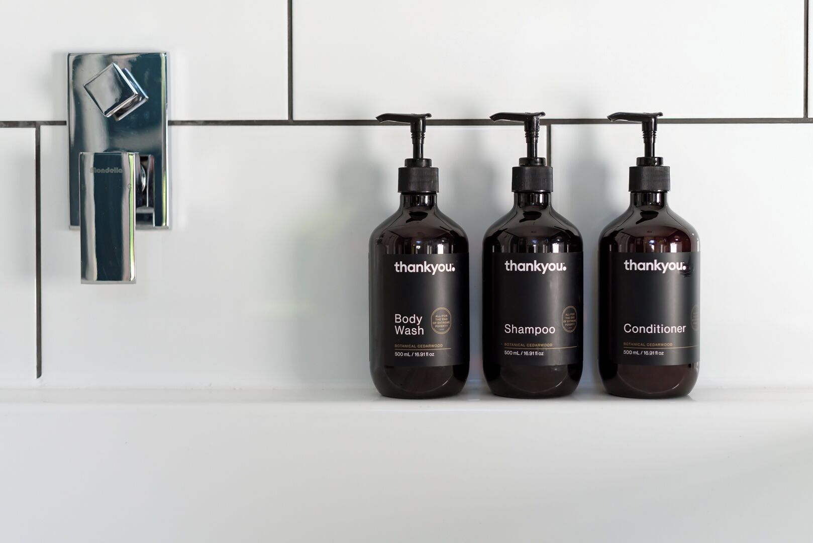 Three bottles of 'thankyou.' body wash, shampoo, and conditioner hanging on a wall.