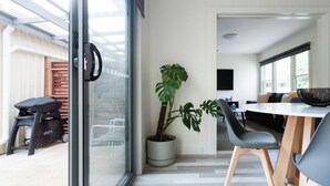 Un interior moderno con un vidrio que da a un espacio exterior, una planta en maceta, una mesa de comedor con sillas y un sofá.