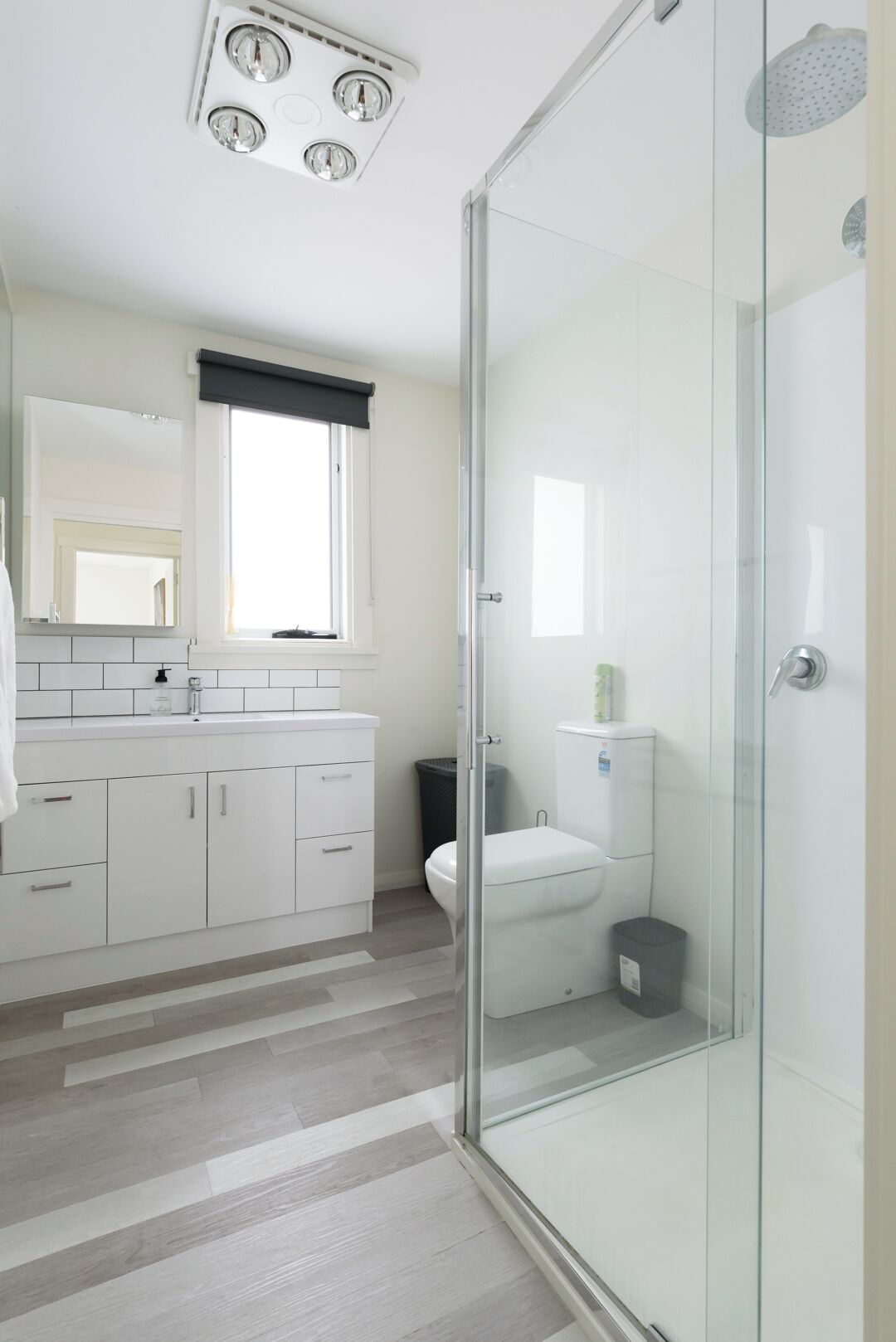 A modern bathroom with a glass shower enclosure, white cabinetry, and a large mirror above the sink.