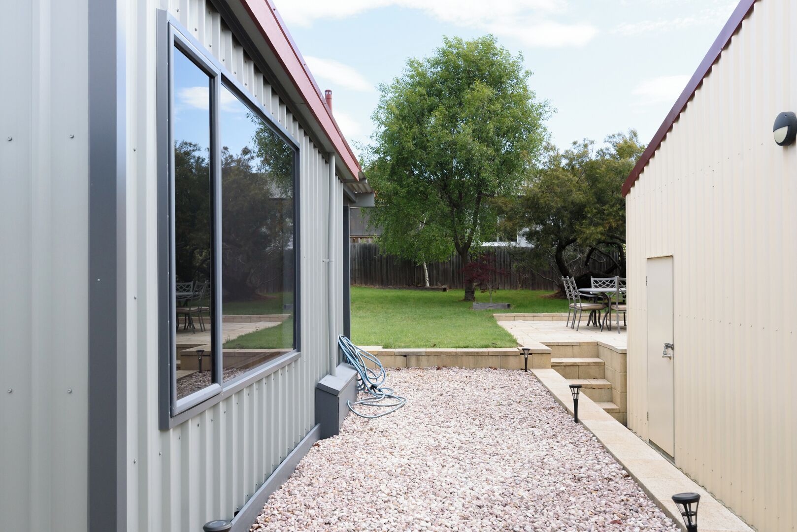Un espace patio avec un sol en gravier, une clôture en métal et un arbre en arrière-plan.