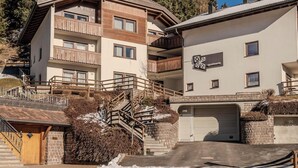 Un edificio residencial de varios pisos con un balcón de madera, un garaje y una escalera que lleva a la entrada.