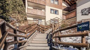 Un hotel de varios pisos con balcones de madera, una escalera que lleva a la entrada y un letrero que indica que es una propiedad vacacional.