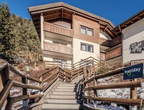 A multi-story building with wooden balconies, a staircase leading to the entrance, and a sign indicating 'holiday apartments'. - Hotiday Apartments Santa Cristina (Santa Cristina Val Gardena)