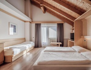 A modern hotel room with a wooden ceiling, two beds, a desk, and a large window with curtains. - Hotiday Apartments Santa Cristina (Santa Cristina Val Gardena)