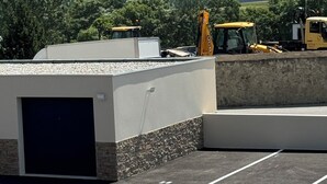 Ein Parkplatz mit einem Gebäude im Vordergrund und Baufahrzeugen im Hintergrund.