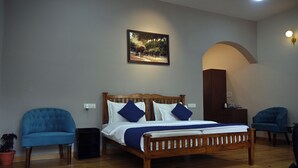 A bedroom with a wooden bed, two blue armchairs, a potted plant, and a painting on the wall.