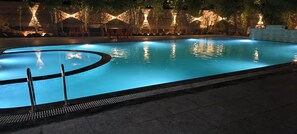 Piscina com borda curva, cercada por um muro de pedra e árvores.