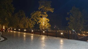 A paved outdoor area with a metal fence, trees, and a well-lit pathway.
