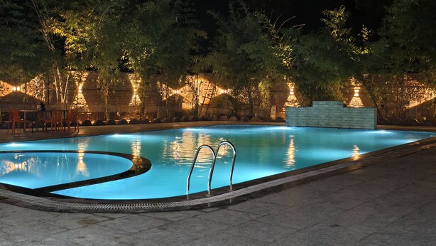 A nighttime swimming pool with surrounding trees and a brick wall.