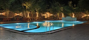 Une piscine éclairée pour la baignade nocturne, entourée d ’arbres et bordée d’un mur de briques.