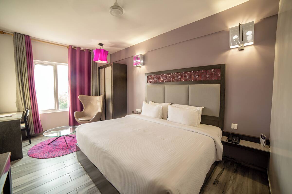 Ein Hotelzimmer mit einem großen Bett, einem Schreibtisch, einem Stuhl und einem Fenster mit Vorhängen.