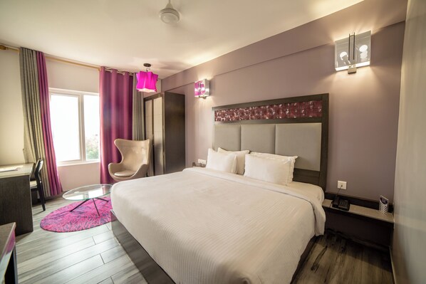 A hotel room with a large bed, a desk, a chair, and a window with curtains. - Hotel Visakka - Palani (Palani)