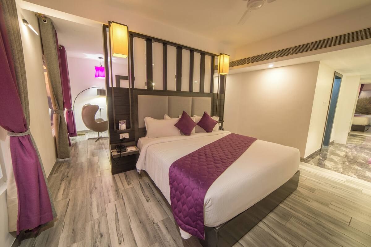 Ein modernes Hotelzimmer mit einem großen Bett, einem Nachttisch, einem Sessel und Blick auf den Flur.