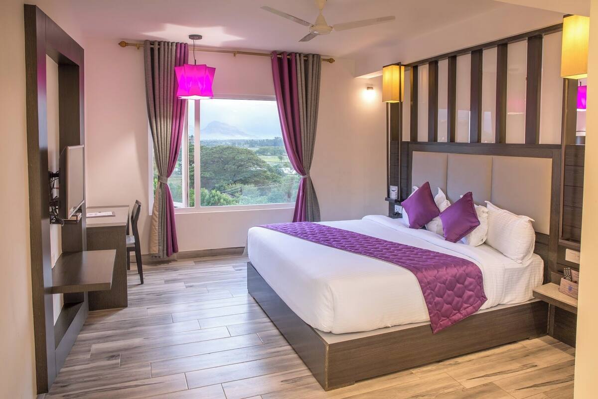 Ein Hotelzimmer mit einem großen Bett, einem Schreibtisch und Blick auf Grünflächen.