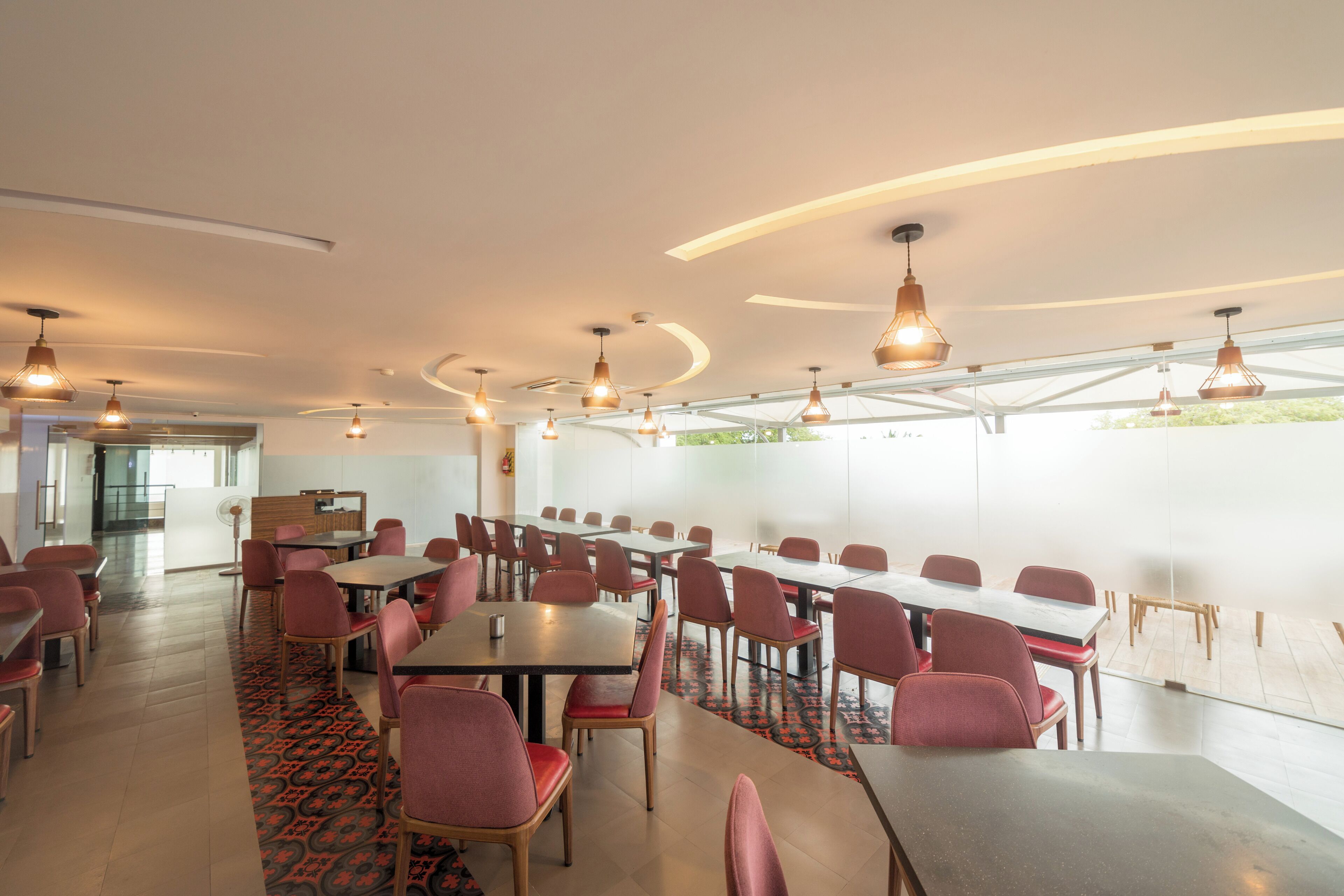 A spacious conference room with multiple tables and chairs, large windows, and pendant lighting.